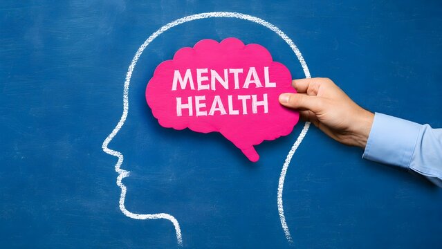 Hand placing a pink brain cutout with text Mental Health inside a chalk-drawn human head silhouette on a blue chalkboard