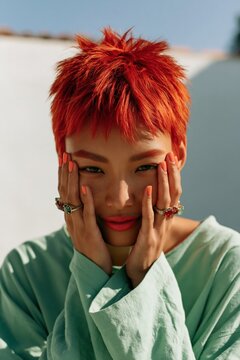 Close fashion portrait of a model with vibrant red pixie haircut and orange manicure wearing mint green top for beauty editorial background and fashion banner design