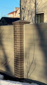 Sunlit brick column by cottage fence, warm golden hour light casts long tree shadows across weathered wooden panels, capstone