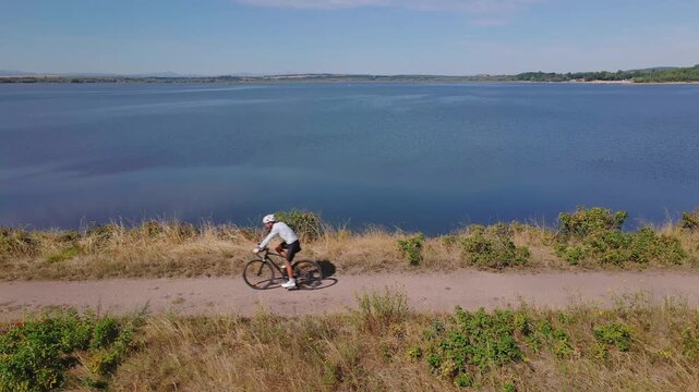 Cyclist riding bicycle on gravel road beside lake