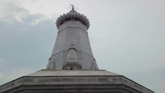 Low angle shot of white marble Hindu temple spire with saffron flag against cloudy sky