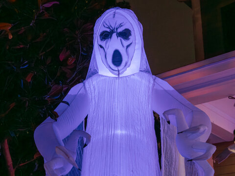 A large illuminated ghost decoration reaches forward in a spooky Halloween display. Purple lighting enhances the eerie nighttime atmosphere.