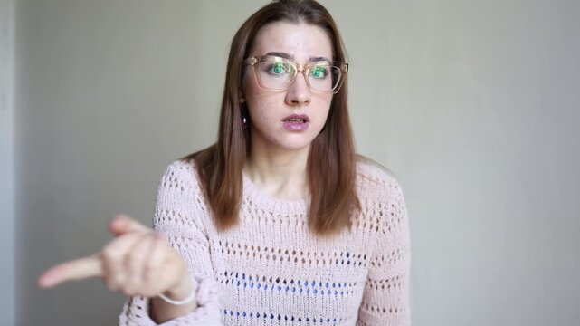 Young woman in glasses raises one index finger while looking at camera with surprised expression giving warning advice reminder or important information to viewer clearly