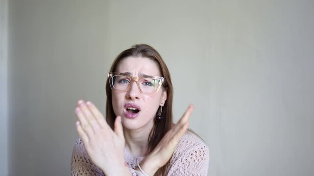 Woman in glasses crosses her arms in a clear stop and no gesture while looking at camera with serious expression showing refusal rejection disagreement and denial indoors