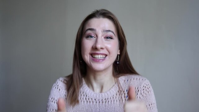 Smiling young woman looks at camera and shows two thumbs up expressing approval success satisfaction positive feedback confidence support and enthusiastic agreement today