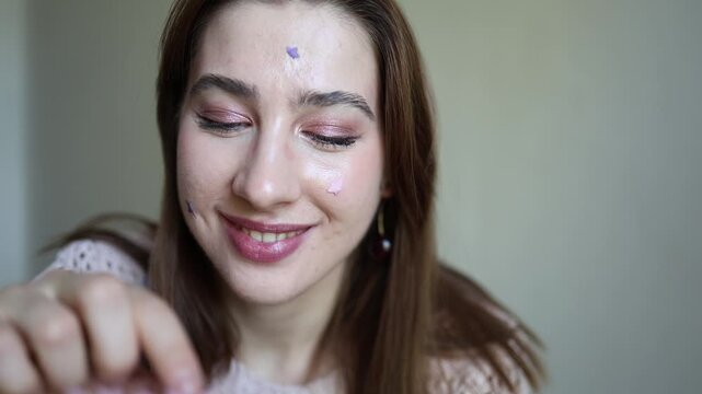 Vertical screen young woman touches cheek while wearing purple star shaped acne patches showing targeted blemish care and a modern daily skincare routine for clearer skin