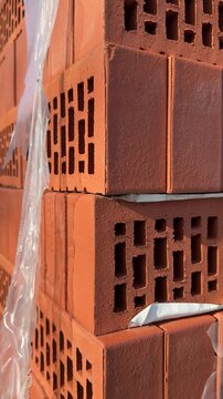 Close-up red bricks stacked outdoors, plastic wrap glistening in sunlight, perforated hollow bricks on pallet at hardware store