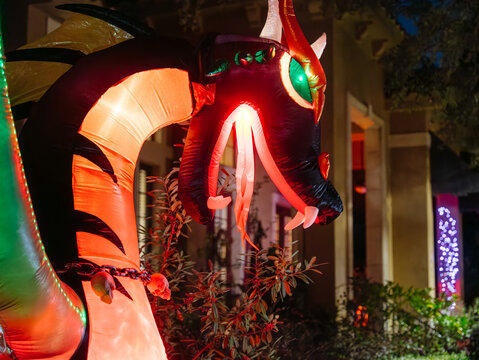 A giant red and black dragon inflatable glows outside a residential building. Bright horns, fangs, wings, and green eyes create a dramatic Halloween display.