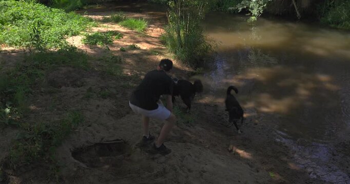 Young man walking his dogs near a muddy river