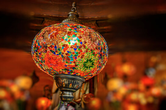A vibrant handmade mosaic lantern glows softly against a warm, dimly lit background.