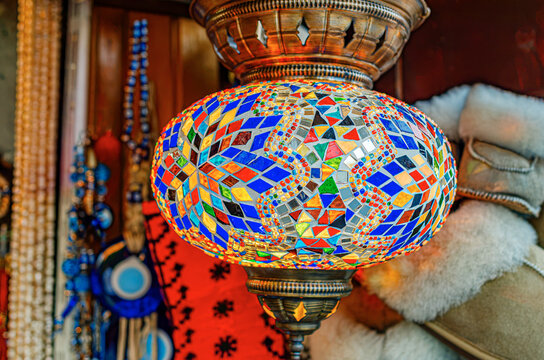 A colorful hand-crafted Turkish mosaic glass lamp hangs glowing in a traditional market shop.