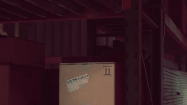 Boxes are stacked on metal shelves in a storage area at night. The lighting creates shadows and highlights the structure of the shelves.