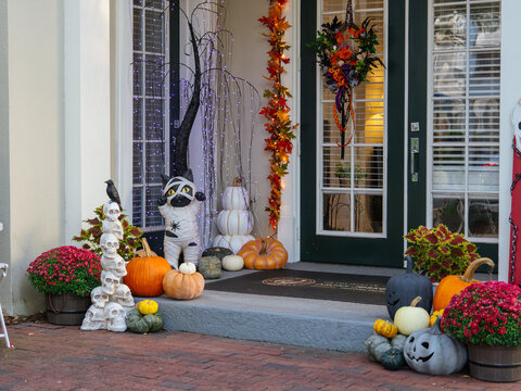 A beautifully decorated front porch features pumpkins, colorful mums, lights, and playful Halloween displays. Seasonal decorations create a warm and inviting autumn entrance.
