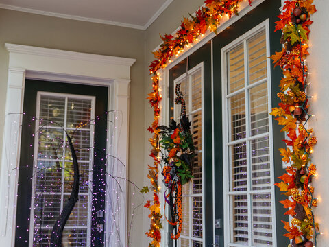 A front entrance is decorated with colorful autumn garlands, glowing string lights, and a festive Halloween wreath. The seasonal display creates a warm and welcoming atmosphere for visitors.