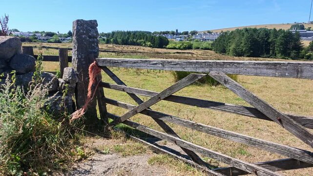 Princetown Dartmoor Devon England UK. 11.08.2026. Video. A weathered wooden gate stands open, revealing charming village of Princetown and the currently used Dartmoor prison.