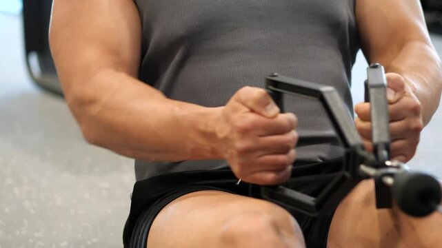 Close-up of a muscular man performing seated cable row exercise with parallel handles for back strength training in a modern gym