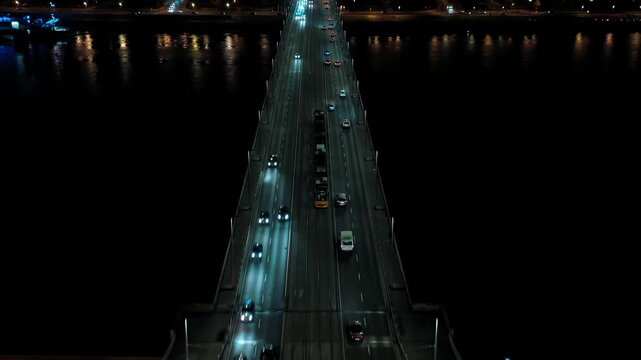 Night drone tracking shot following a tram crossing &Aacute;rp&aacute;d Bridge in Budapest, Hungary, with illuminated city lights and the Danube River below.