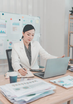 Asian Businesswoman Working on Laptop and Taking Notes at Desk in Office