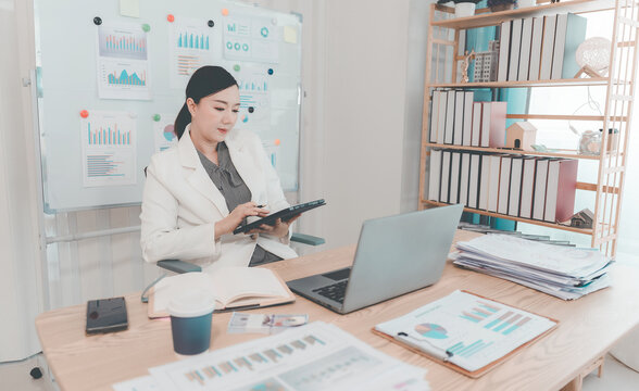 Asian Businesswoman Working on Laptop and Taking Notes at Desk in Office
