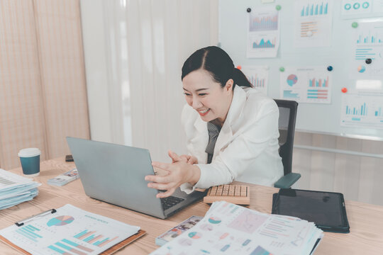 Cheerful Asian Businesswoman Celebrating Success looking at Laptop Screen in Office