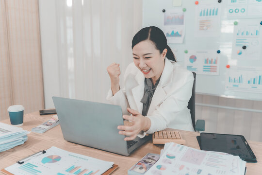 Cheerful Asian Businesswoman Celebrating Success looking at Laptop Screen in Office