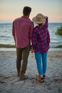 Back view of romantic couple holding hands and looking at lake water on beach