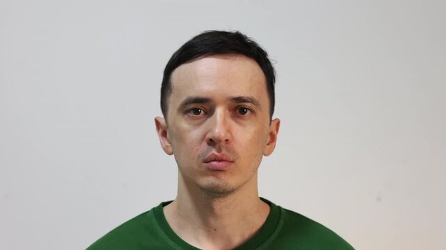 Serious man with a neutral expression looking at the camera while a light moves across his face, creating dramatic changing shadows on a white background, suggesting interrogation or mystery