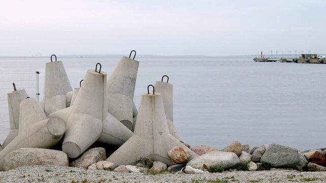 Locked 4K view of concrete wave breakers protecting the shoreline in Tallinn, Estonia, with calm Baltic Sea water and distant harbor infrastructure under an overcast sky.