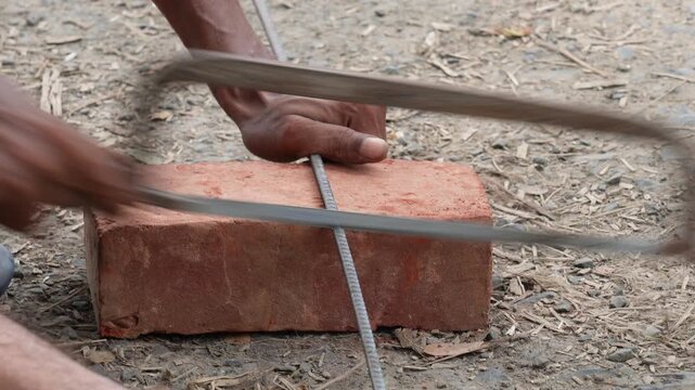 Person cutting metal rebar with a hacksaw on brick