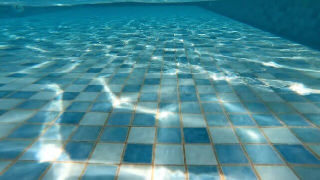 Sunlight shimmering on blue tiled swimming pool bottom underwater