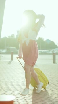 Asian woman moving quickly with suitcase, Traveling woman in vibrant attire with suitcase under sunset light