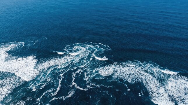Waves crash against the deep blue ocean. White foam forms swirling patterns as the water moves.