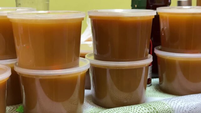 Close-up honey jars on counter warm amber honey in clear plastic containers stacked on cloth market display glossy texture visible