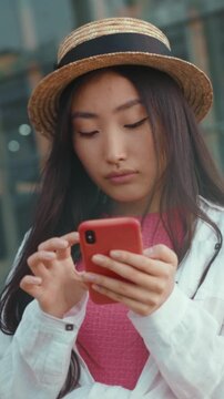 Calm lady browsing outside, Serene young Asian woman in urban setting scrolling her mobile device attentively