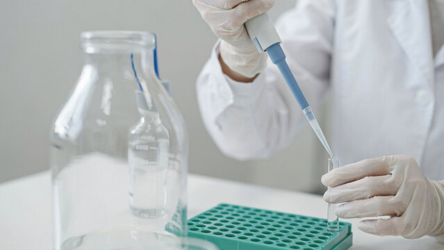 Scientist in white lab coat using pipette for medical research experiment
