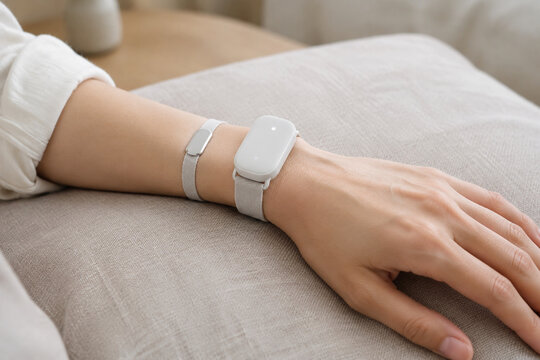 Adult forearm with fabric wristband and silver skin sensor on linen cushion, wearable biofeedback device, health monitoring concept