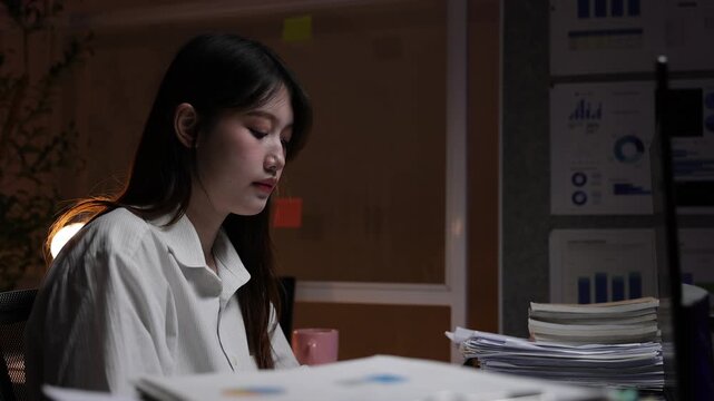 Serious young Asian businesswoman concentrating on her computer screen. A dedicated female employee working overtime in office at night.