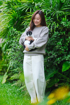 Vertical portrait of a woman holding a black and white colors cat in the garden