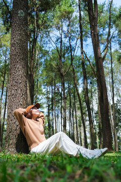 Vertical portrait image of a woman sitting and putting hands behind her neck for relaxing in the park