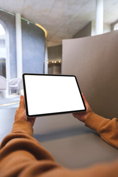 Vertical mockup image of a woman holding digital tablet with blank white desktop screen in cafe