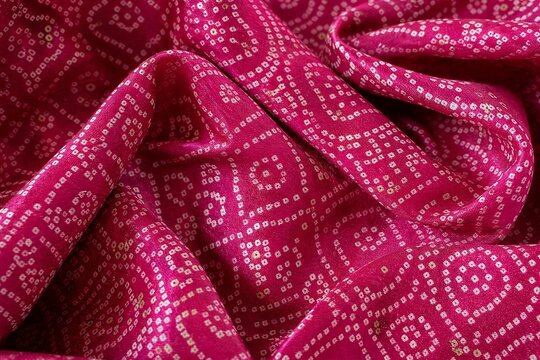 Close-up of traditional Gujarati bandhani tie-dye silk fabric with intricate white dotted circular pattern, soft draped folds, rich magenta texture