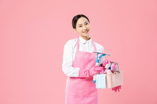 Smiling housekeeper holding cleaning supplies on pink background