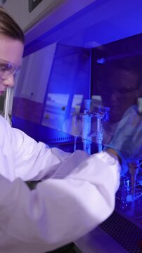 Scientist in laboratory using a pipette and test tube rack under uv light. Female scientist in a modern laboratory conducting experiment under a biosafety cabinet.