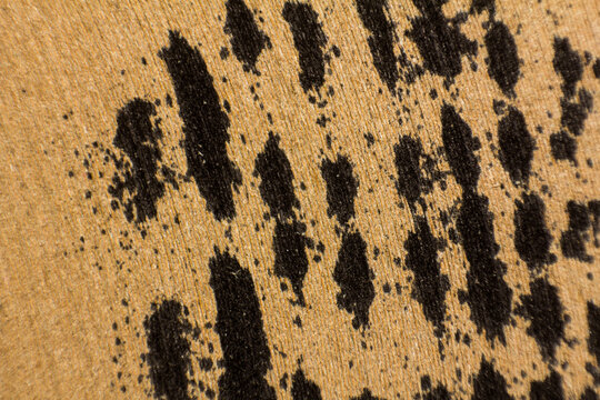 Close-up macro photography of black charcoal textured marks on a rough light brown paper surface backdrop