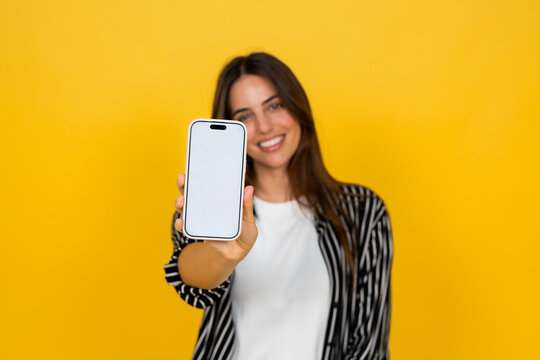 Smiling woman showing smartphone to camera on bright yellow background for mobile marketing