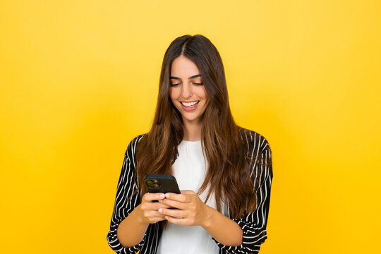 Young happy woman actively engaging with her smartphone, enjoying digital communication and social media on a vibrant yellow background, representing connection and modern technology use