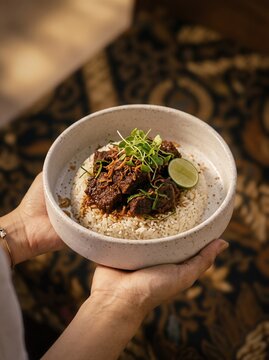 Nasi Rendang. Nasi Rendang daging sapi. Indonesian Beef Rendang with Rice Bowl. Nasi Rendang Tangan Memegang. Person Holding Bowl of Delicious Indonesian Beef Rendang with Rice over Batik Backgraund 