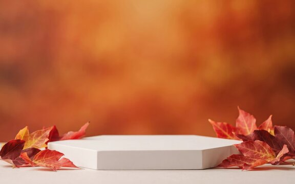 White hexagonal display platform with autumn leaves on blurred orange background