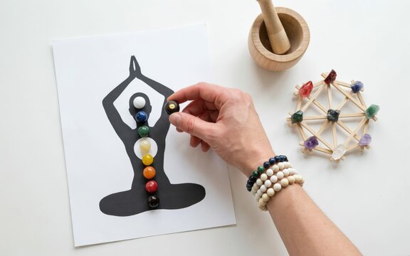 Hand placing gemstone on yoga chakra with crystal grid