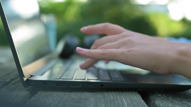 Side view of female hands typing on laptop keyboard at park table.